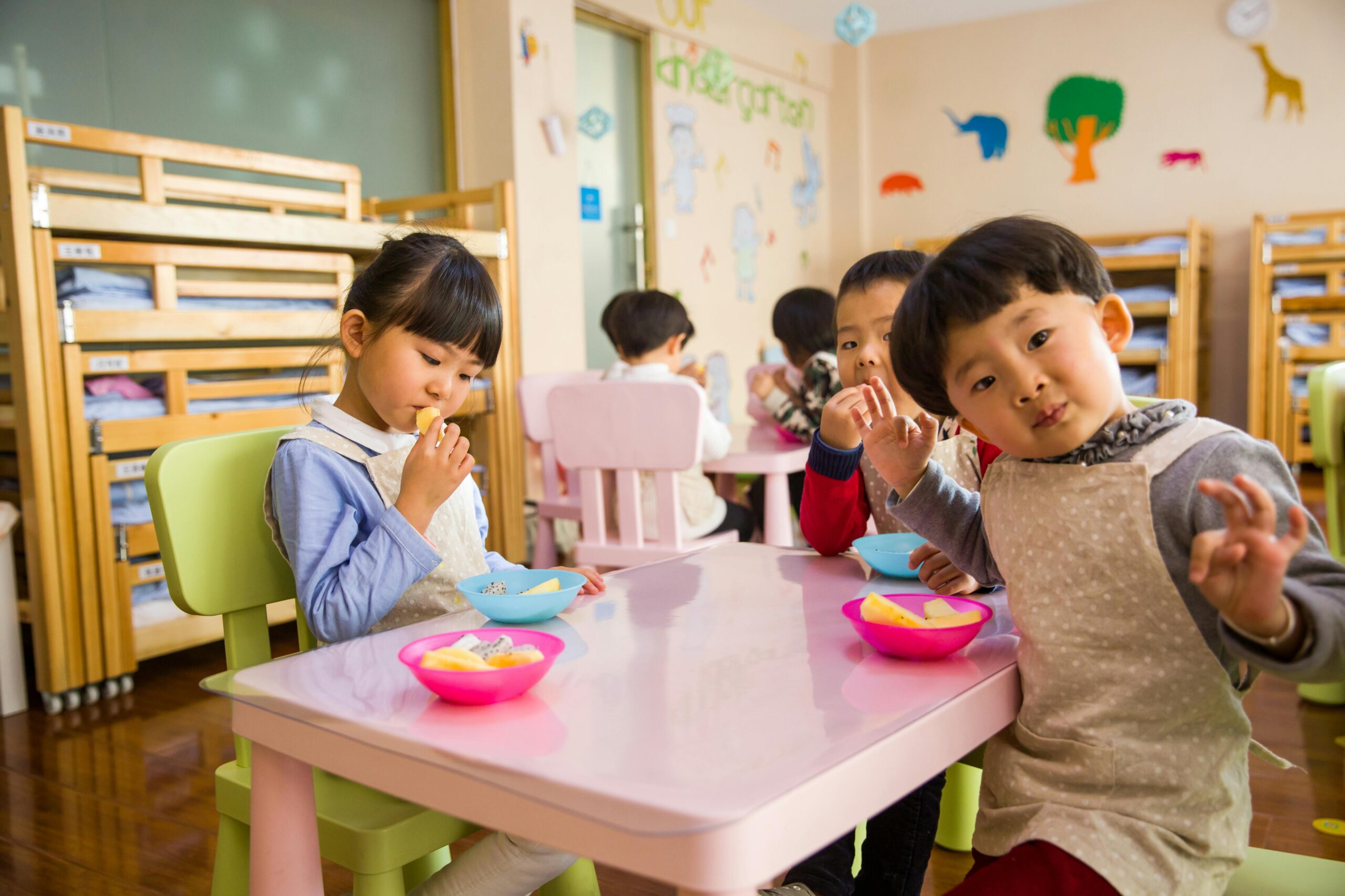 Kids seated around a table in a colorful classroom, eating snacks happily.