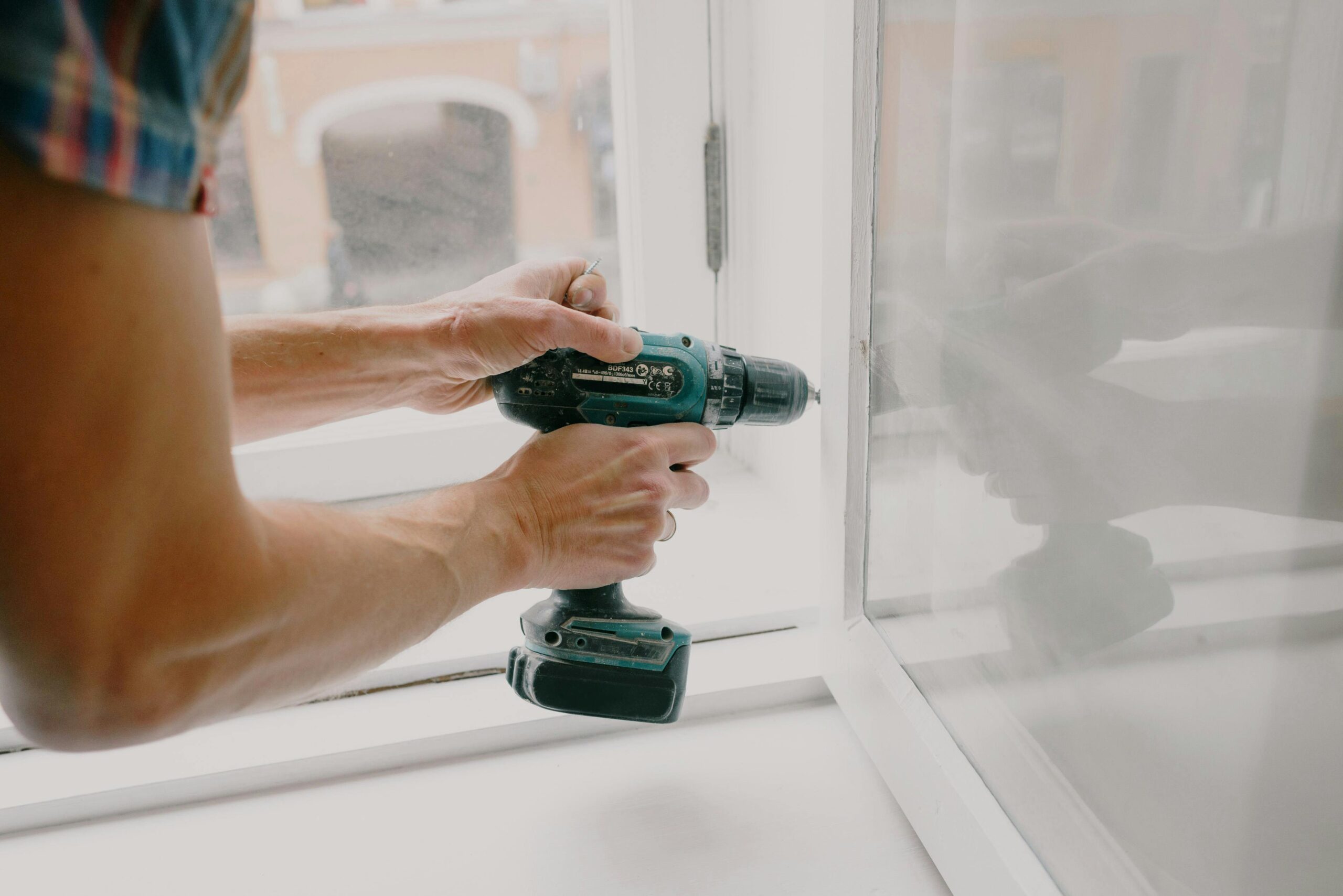 A person using an electric drill to repair or install a window indoors.